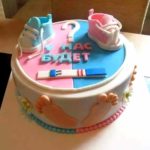 Розово-синий торт, украшенный пинетками, тестом на беременность и надписью «У нас будет»
