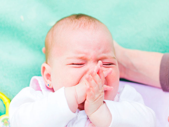 Новорождённый ребёнок закрыл ручками лицо и сожмурился