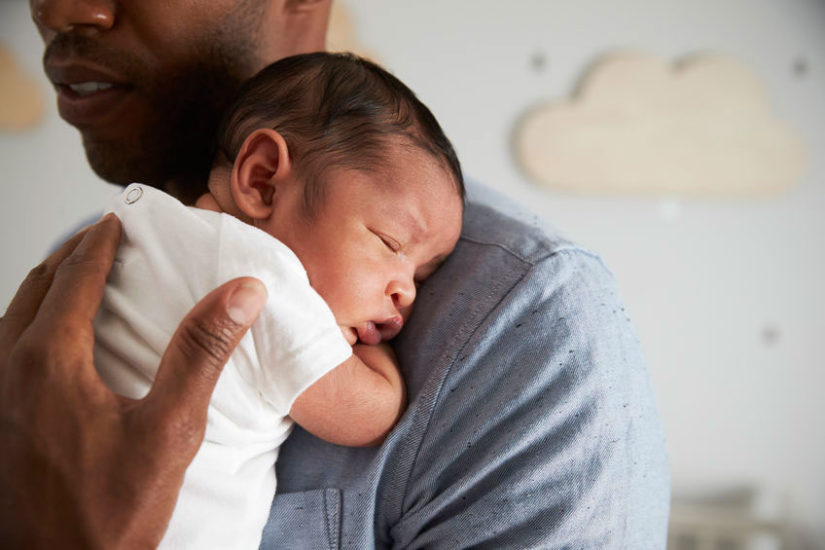 father carrying newborn on shoulder