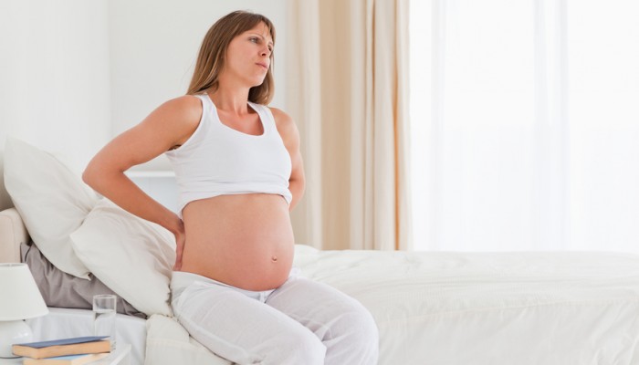 Attractive pregnant female having a back pain while sitting on a bed in her apartment