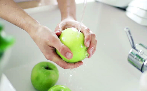 Руки тщательно моют зелёные яблоки под краном