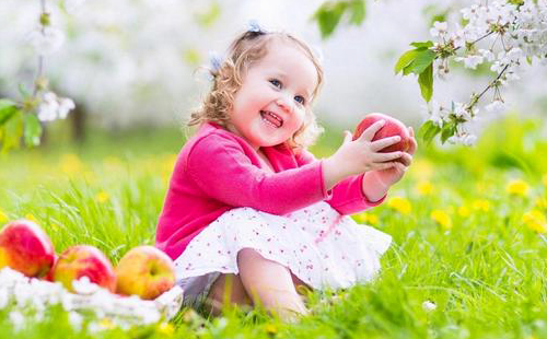 Девочка в розовой кофточке держит яблоко и смеётся