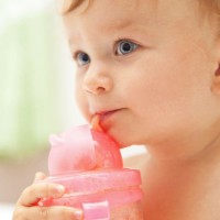Задумчивый младенец пьёт воду из розового поильника