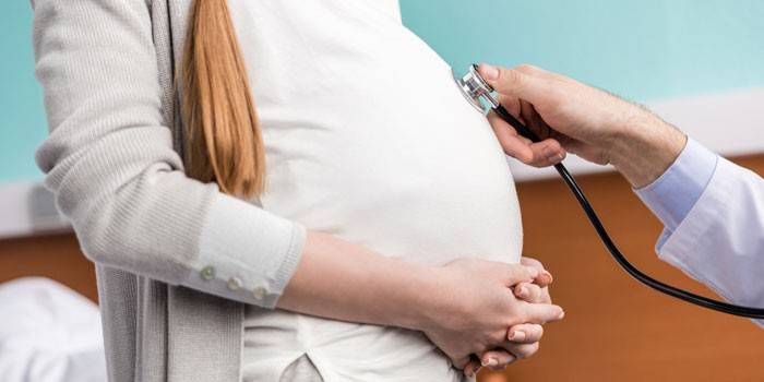 Медик слушает сердцебиение плода у беременной девушки