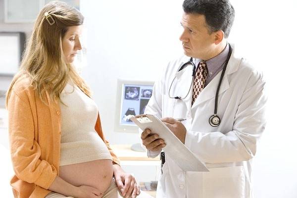 Медик слушает сердцебиение плода у беременной девушки