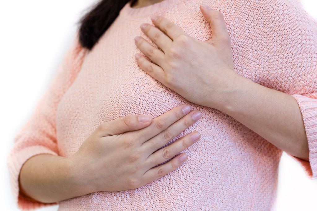 Женщина в розовой кофте держится руками за грудь