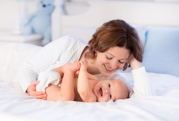 Веселый младенец с мамой на кровати