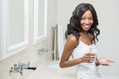 Beautiful woman holding pill and glass of water