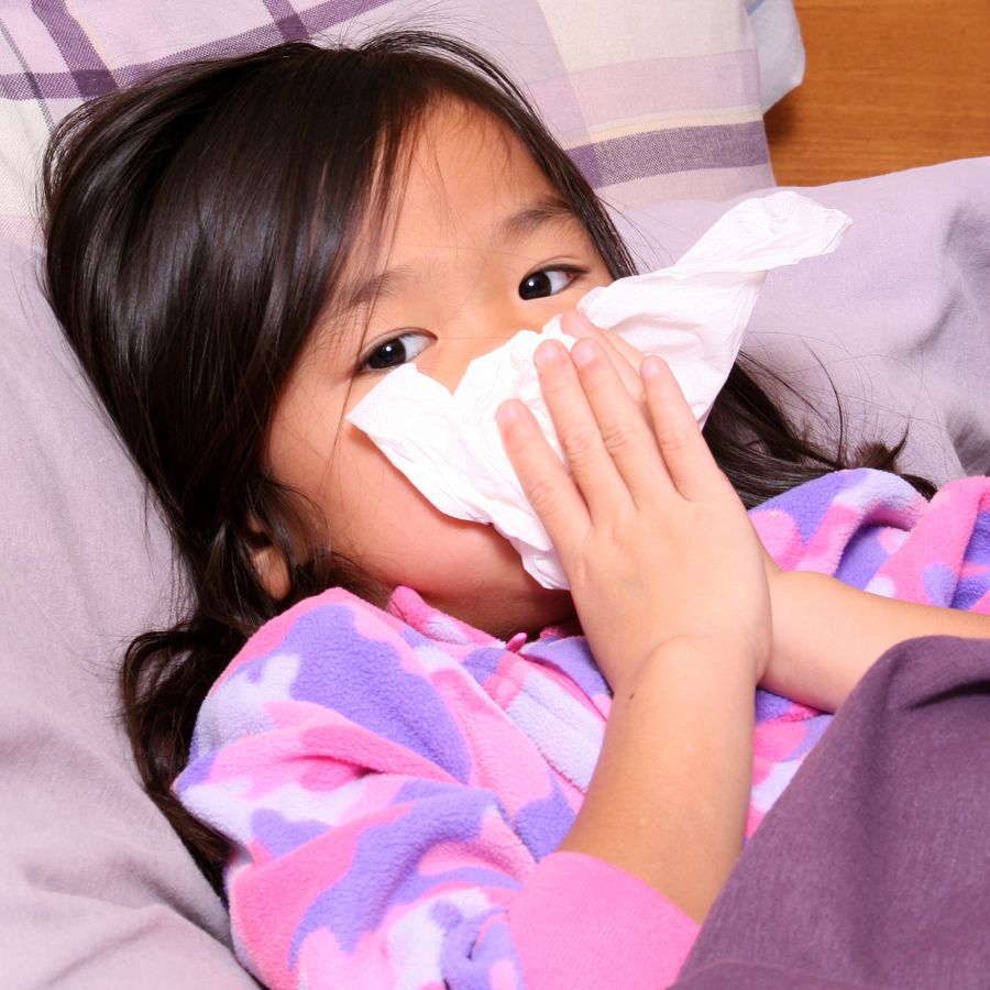 Child blowing her nose, sick in bed with a cold.